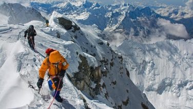Alt text: Mount Everest climbers battling icy winds and steep slopes, surrounded by mist and clouds.