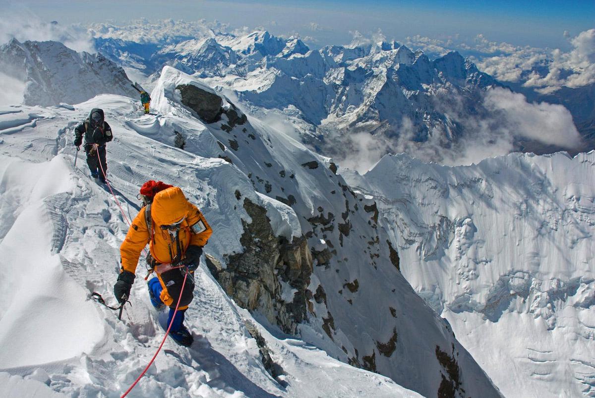 Alt text: Mount Everest climbers battling icy winds and steep slopes, surrounded by mist and clouds.