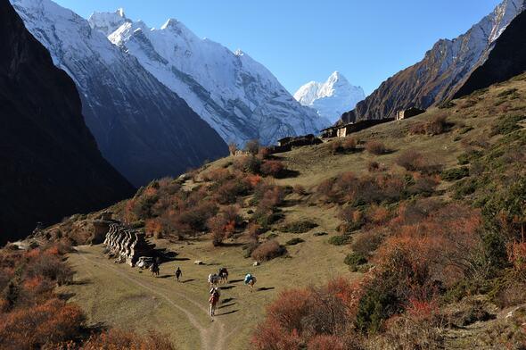 Lone hiker before Mount Everest at dawn, with prayer flags and vivid Himalayan landscape.
