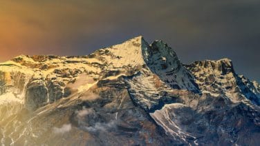 Solo traveler stands contemplatively by a serene lake, Himalayas towering in the background.