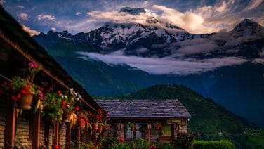 a house with flowers and mountains in the background in annapurna base camp trek