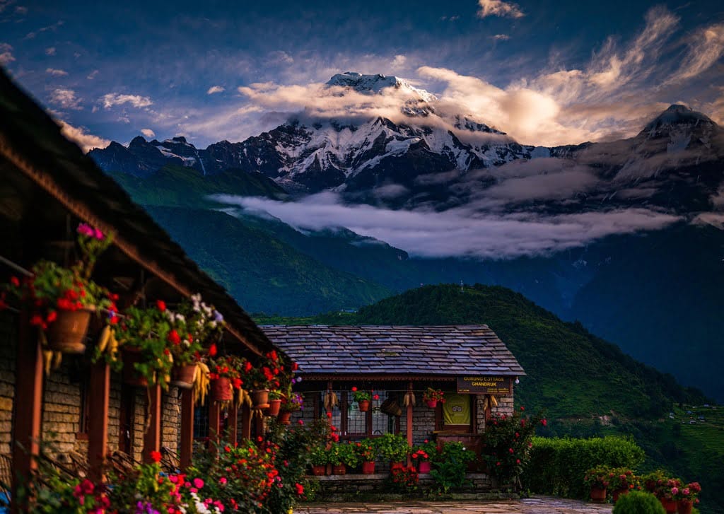a house with flowers and mountains in the background in annapurna base camp trek