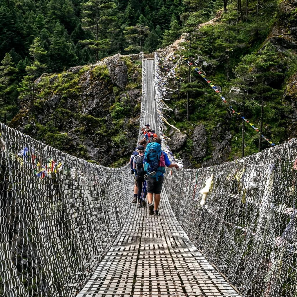 a group of people walking on a suspension bridge during everest base camp trek