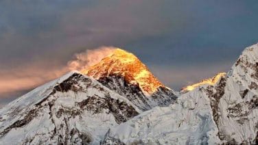 Climber ready to ascend Mount Everest in crisp morning light, amid increased fees.